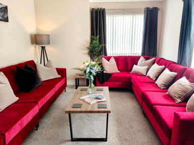 A living room with red sofas beige pillows a wooden coffee table with flowers and magazines at The Paddock in Keswick