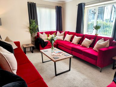 A living room with two red sofas a wooden coffee table with a vase of flowers and magazines at The Paddock in Keswick