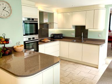 A kitchen with white cabinets a microwave a sink ovens a countertop with fruit bowls and a clock on the wall at The Paddock in Keswick
