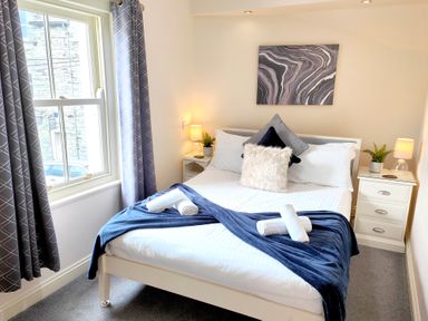 A bedroom with a bed with pillows and folded towels and two bedside tables with lamps at The Paddock in Keswick