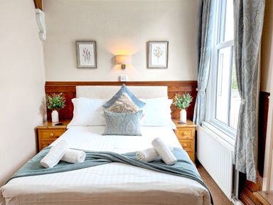 A bedroom with a bed with pillows and rolled towels beside a window with curtains at The Paddock in Keswick