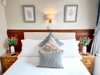 A bed with three pillows and two nightstands with vases of greenery at The Paddock in Keswick