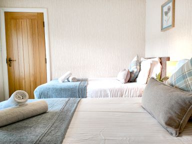 A bedroom with two single beds with pillows and rolled towels near a wooden door at The Paddock in Keswick