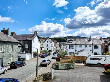 A street with parked cars and white houses under a blue sky with clouds