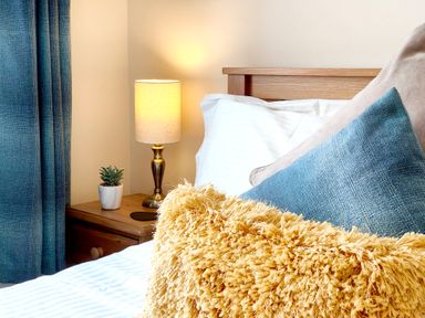 A bedroom with a bed with pillows next to a bedside table with a lamp and plant at The Paddock in Keswick