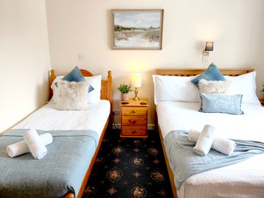 A bedroom with two beds separated by a wooden nightstand with a lamp and a plant at The Paddock in Keswick