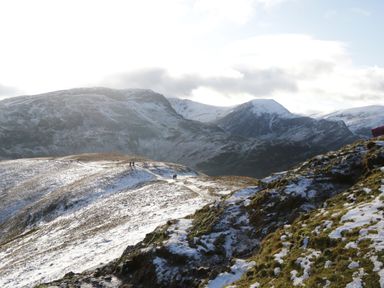 A mountainous landscape with snow patches and people walking on a trail