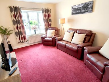 A living room with red leather sofas a floor lamp curtains at The Paddock in Keswick