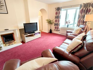 A living room with leather sofas a television on a wooden stand a fireplace and patterned curtains at The Paddock in Keswick