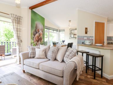 A living room with a sofa and cushions next to a dining area with a table and chairs at Nutkins Lodge in Beckside 5 Limefitt Park near Windermere