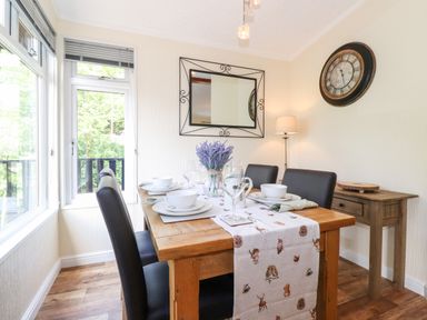 A dining area with a wooden table set for four with bowls and glasses and a floral centerpiece at Nutkins Lodge Beckside 5 Limefitt Park near Windermere