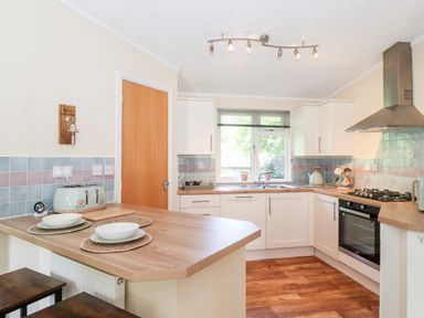 A kitchen with white cabinets wooden countertops a toaster a kettle and a gas stove at Nutkins Lodge in Beckside 5 Limefitt Park near Windermere