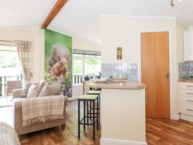 A living area with a sofa and cushions near a kitchen counter with stools at Nutkins Lodge Beckside 5 Limefitt Park near Windermere