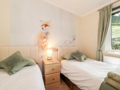 A bedroom with two single beds a nightstand with a lamp and a fox mural on the wall at Nutkins Lodge Beckside 5 Limefitt Park near Windermere