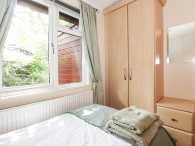 A bedroom with a bed covered by folded towels a wardrobe a chest of drawers and a window with curtains at Nutkins Lodge Beckside 5 Limefitt Park near Windermere