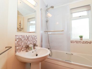 A bathroom with a sink, mirror, bathtub with shower and a window with a small plant at Nutkins Lodge Beckside 5 Limefitt Park near Windermere