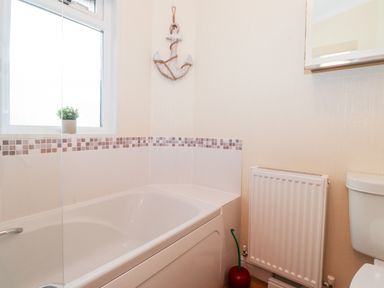 A bathroom with a bathtub a window with a small plant a radiator a toilet and an anchor decoration on the wall at Nutkins Lodge Beckside 5 Limefitt Park near Windermere