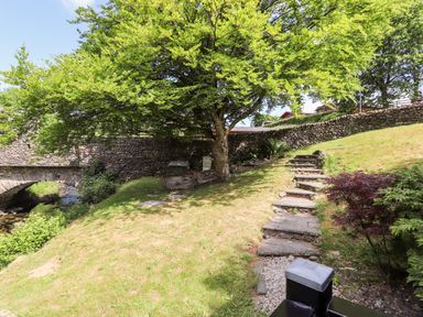 A garden with stone steps leading uphill beside a tree and stone wall at Nutkins Lodge Beckside 5 Limefitt Park near Windermere