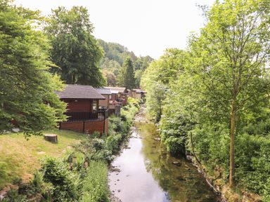 A river flowing between trees and houses at Nutkins Lodge in Beckside 5 Limefitt Park near Windermere