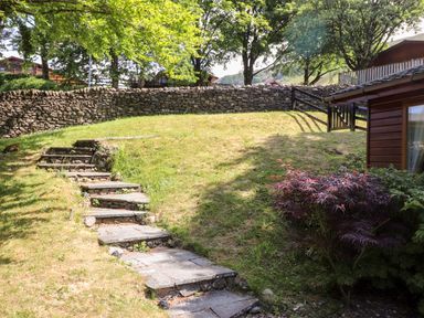 A stone pathway leads up a grassy hill with a stone wall and wooden gate at Nutkins Lodge in Beckside 5 Limefitt Park near Windermere