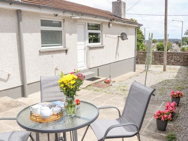 A patio area with a round glass table and two chairs outside a bungalow at Apple Tree Bungalow in Lanner