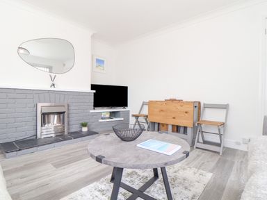A living room with a gray brick fireplace a round coffee table two folding chairs and a TV on a wall shelf at Apple Tree Bungalow in Lanner