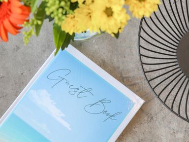 A guest book on a table with a vase of flowers and a decorative wire bowl at Apple Tree Bungalow in Lanner