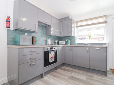 A kitchen with grey cabinets a built-in oven a turquoise microwave kettle and toaster and a window with blinds at Apple Tree Bungalow in Lanner