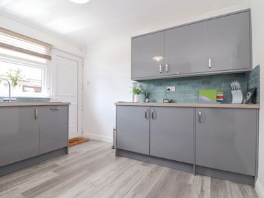 A kitchen with grey cabinets green tiled backsplash and a window by the door at Apple Tree Bungalow in Lanner