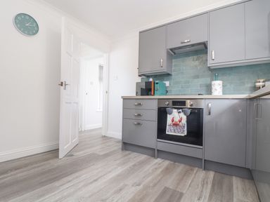 A kitchen with grey cabinets a microwave an oven with a crab towel and a wall clock at Apple Tree Bungalow in Lanner