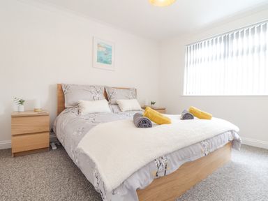 A bedroom with a bed with gray patterned bedding and pillows two wooden bedside tables and a window with vertical blinds at Apple Tree Bungalow in Lanner
