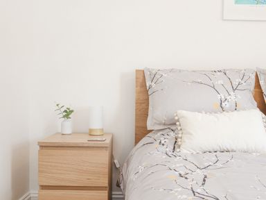 A bedroom with a wooden nightstand holding a small plant and lamp next to a bed with floral bedding at Apple Tree Bungalow in Lanner