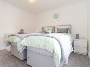 A bedroom with two single beds side by side with green patterned bedding and rolled towels on top at Apple Tree Bungalow in Lanner