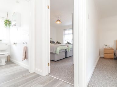 A hallway with a view into a bathroom with a toilet and a bedroom with two beds at Apple Tree Bungalow in Lanner