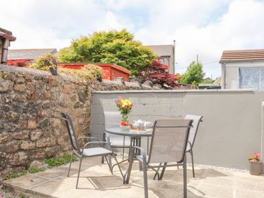 An outdoor patio with a glass table four chairs a vase with flowers and a stone wall at Apple Tree Bungalow in Lanner