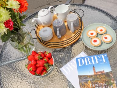 A glass table with a flower vase strawberries tea set tarts and magazines at Apple Tree Bungalow in Lanner