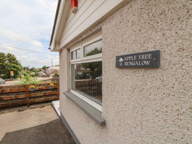 The exterior wall of a building with a sign reading apple tree bungalow and a window with a wooden fence and flowers in the background at Apple Tree Bungalow in Lanner