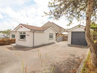 A bungalow with a detached garage a paved driveway and a tree at Apple Tree Bungalow in Lanner
