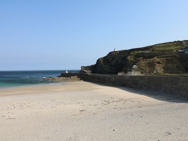A sandy beach with a concrete seawall and rocky cliffs by the ocean at Apple Tree Bungalow in Lanner