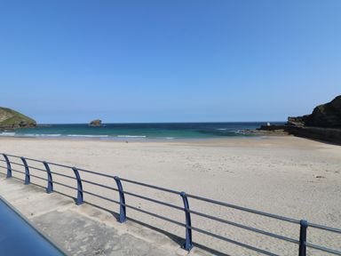 A sandy beach with a metal railing and ocean waves at Apple Tree Bungalow in Lanner
