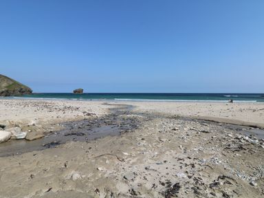 A sandy beach with a small stream flowing to the sea and people near the water at Apple Tree Bungalow in Lanner