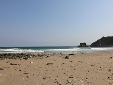 A sandy beach with scattered rocks and waves in the sea near a rocky cliff with a small white lighthouse at Apple Tree Bungalow in Lanner