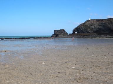 A sandy beach with people walking near rocky cliffs and a blue sky at Apple Tree Bungalow in Lanner