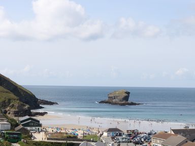 A beach with people on the sand and in the water with a large rock formation offshore at Apple Tree Bungalow in Lanner