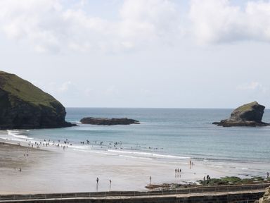 A beach with people on the shore and in the water near rocky cliffs and outcrops at Apple Tree Bungalow in Lanner
