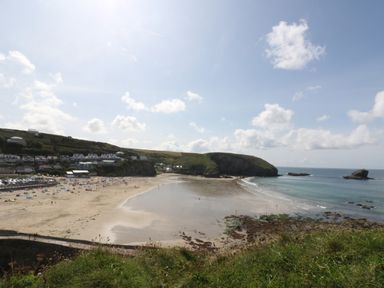 A sandy beach with people on the shore and houses on a hillside in the background at Apple Tree Bungalow in Lanner