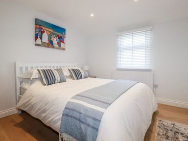 A bedroom with a white bed frame and a bed with pillows and a blanket in front of a window at Beach Cottage in Cadgwith