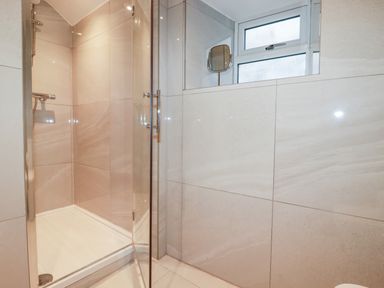 A shower area with glass door tiles and a window with a small mirror in a bathroom at Beach Cottage in Cadgwith