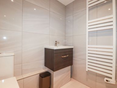 A bathroom with a toilet a sink with a cabinet a small trash bin and a heated towel rail at Beach Cottage in Cadgwith