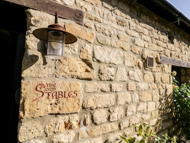 A stone exterior wall with a light fixture and a sign that reads The Old Stables at The Old Stables in Chipping Campden